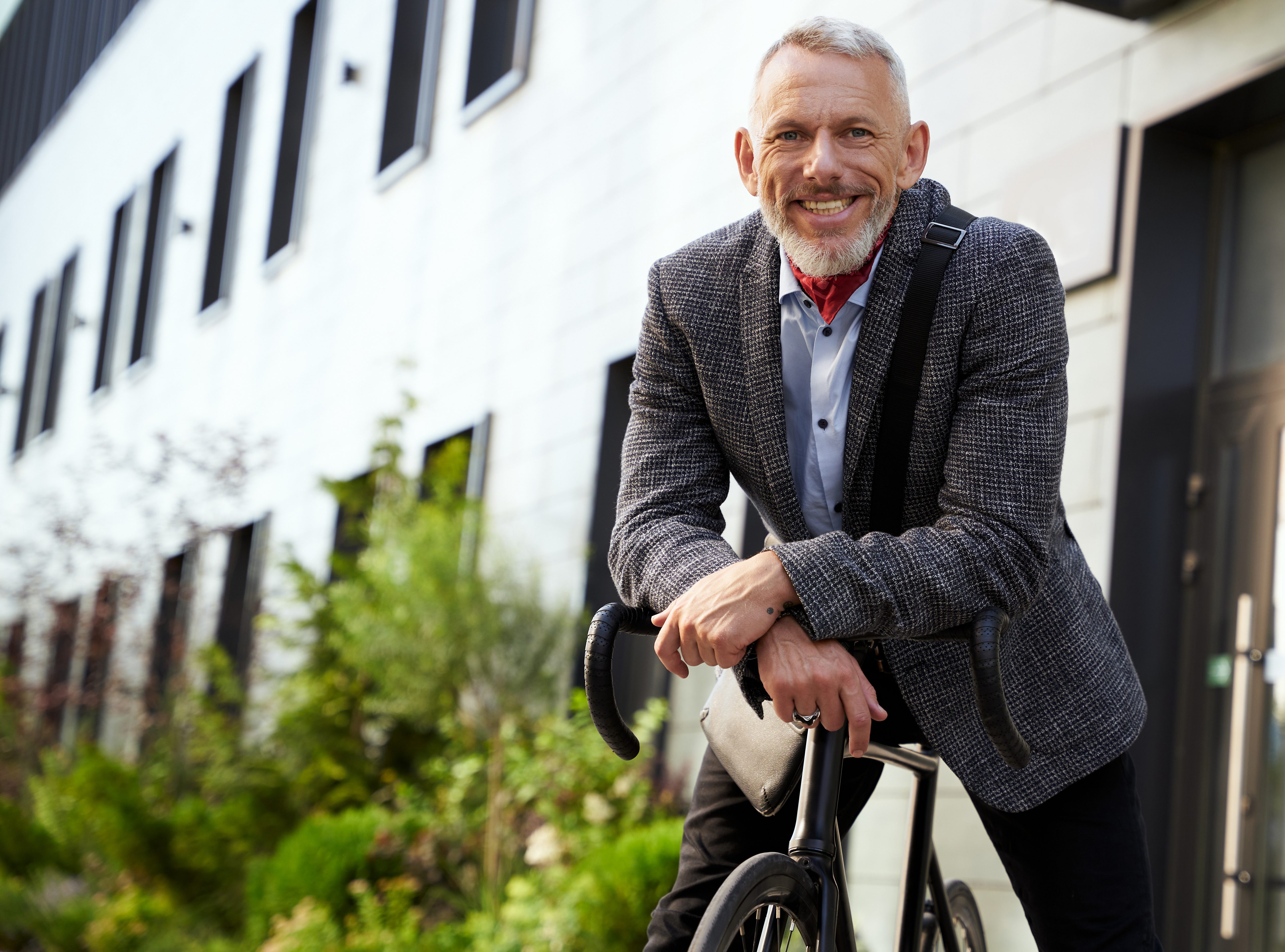 Confident, stylish mature businessman smiling at camera while standing with his bicycle outdoors on