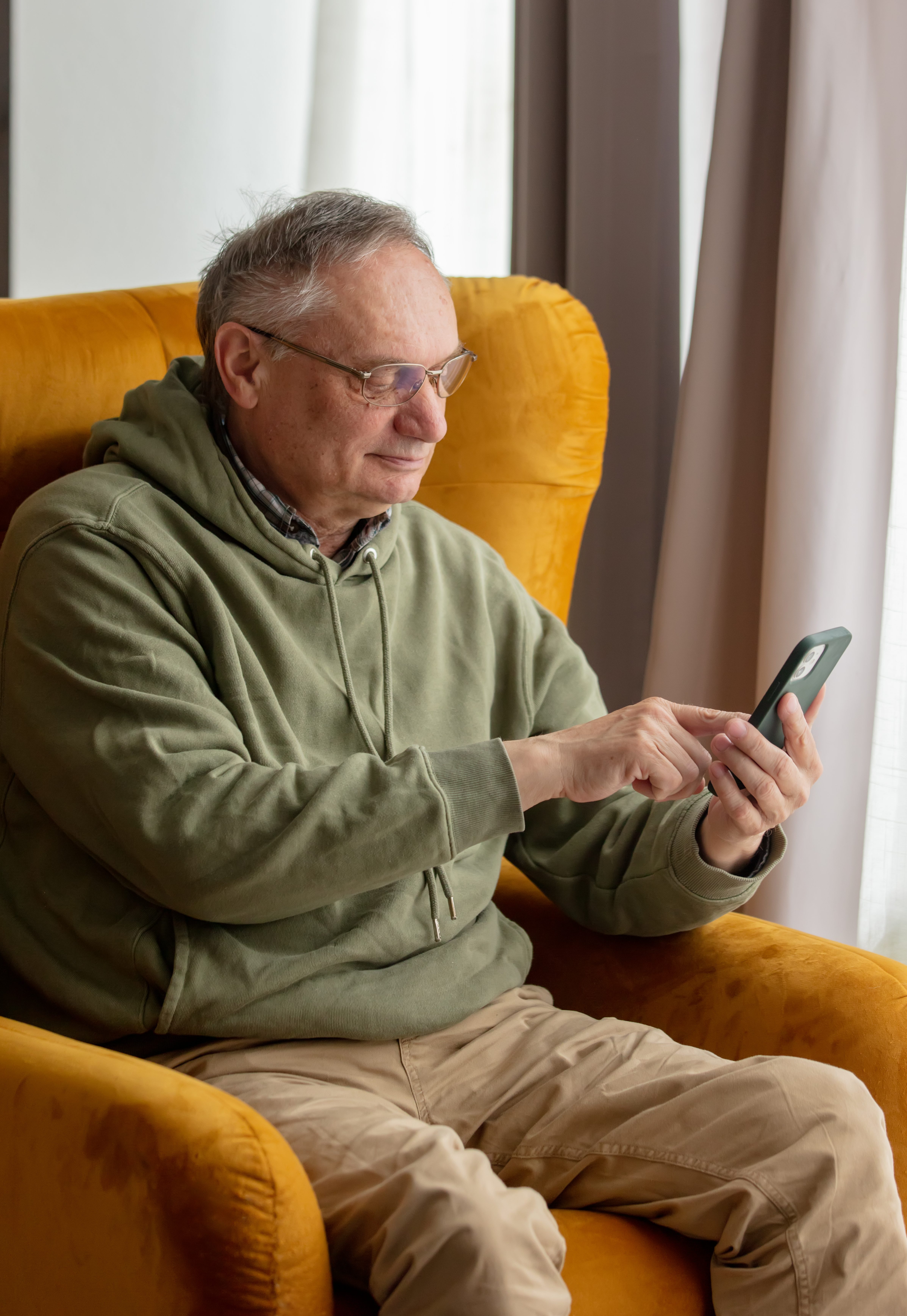 Senior male sits in armchair at home and using mobile phone