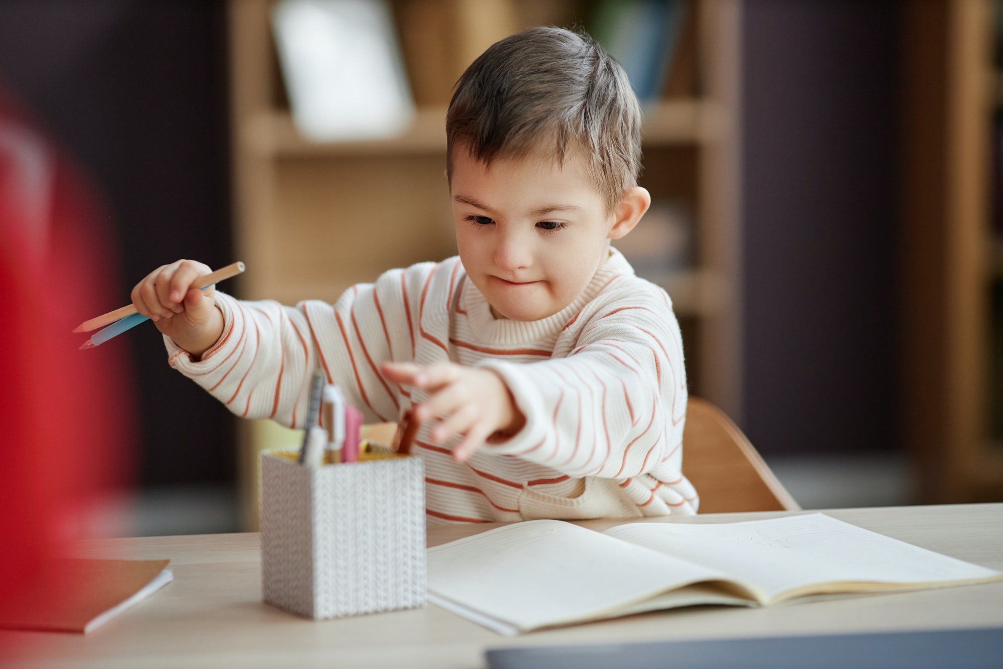 Excited little boy with down syndrome drawing pictures at home